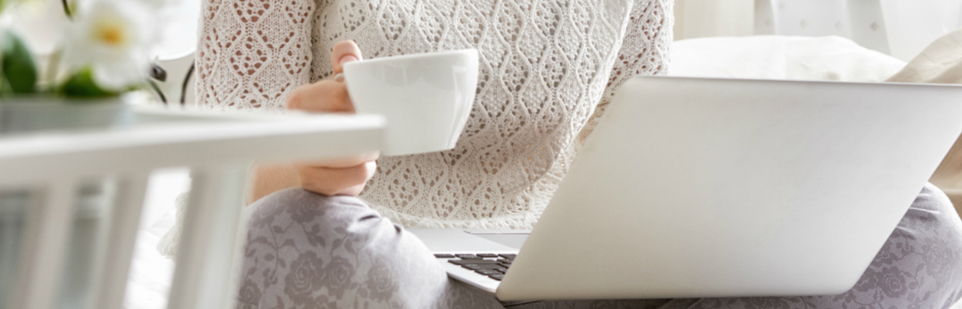 A woman sitting cross legged with a cup of tea and a laptop.